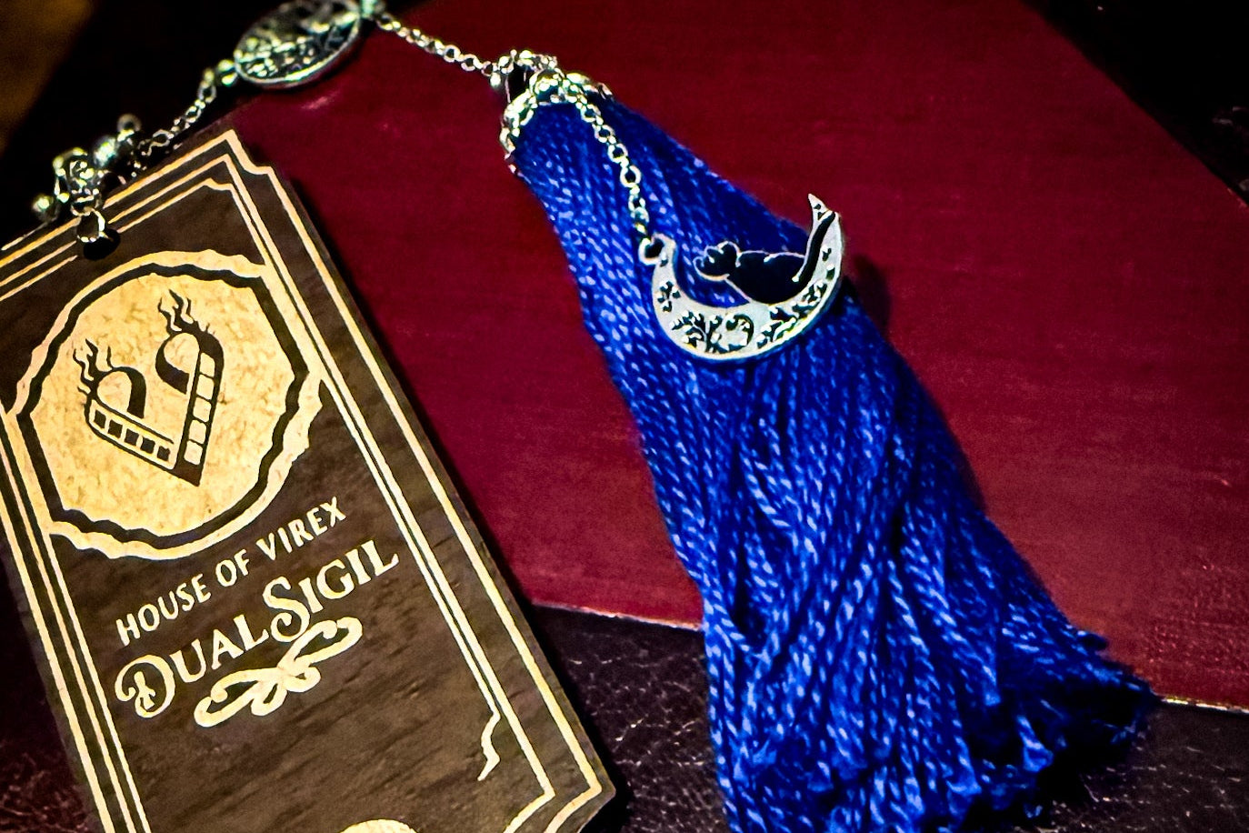 Bookmark with the dual sigil logo and with purple tassel attached 