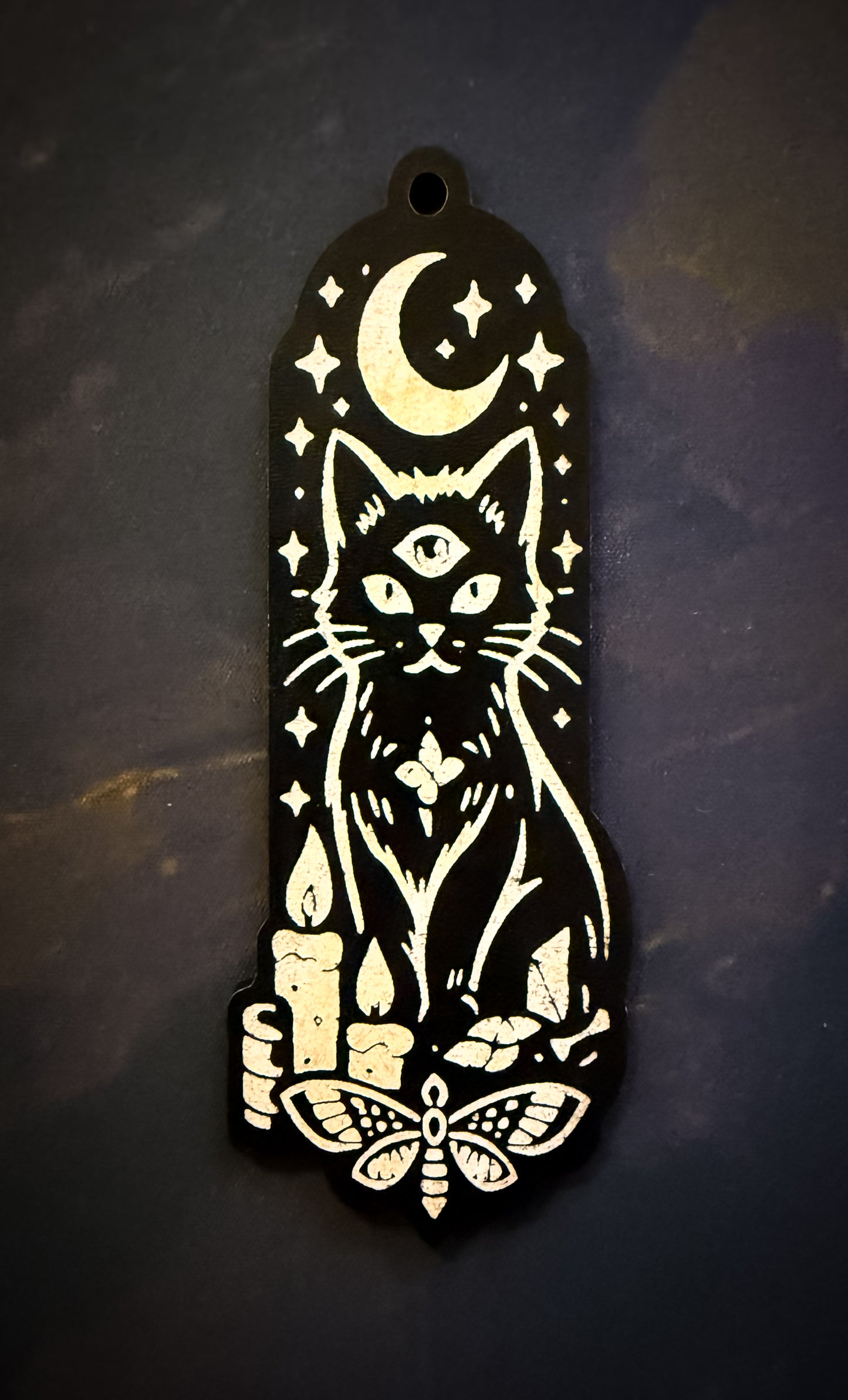 Decorative black and white pendant with a cat, moon, and candles design on a dark background.