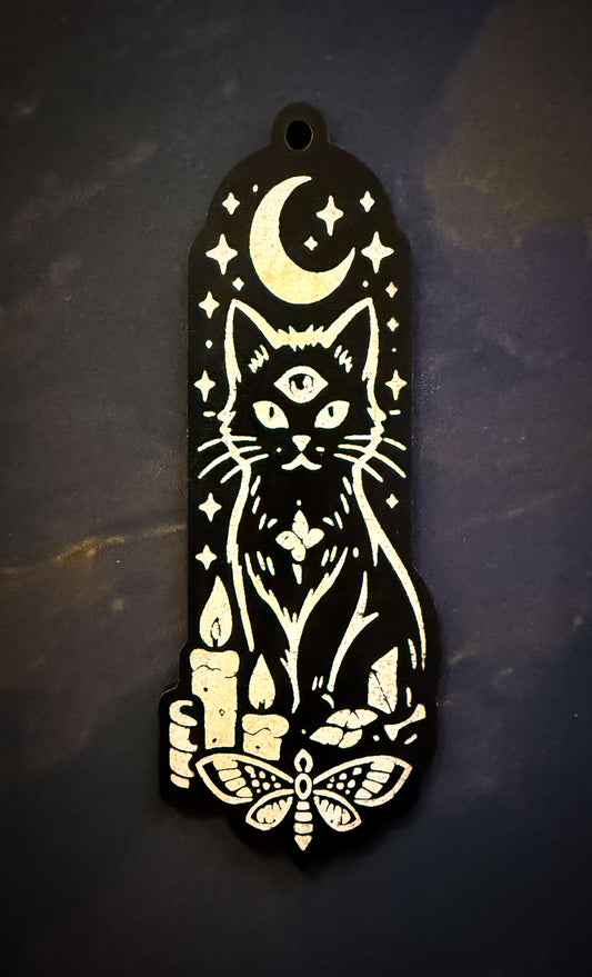 Decorative black and white pendant with a cat, moon, and candles design on a dark background.